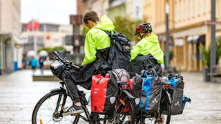 Zwei Radtouristen stehen bei Regen mit ihren Fahrrädern in einer Fußgängerzone (Symbolbild).
