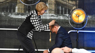 Christian Specht auf den Knien, als Marianne Seitz dem Oberbürgermeister die Amtskette umhängt.