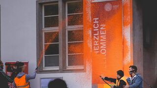 Orange Revolution? Mit Feuerlöschern rennen Klimaaktivisten auf die Fassade der Universität zu.