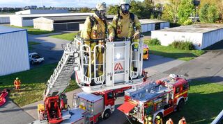 Großübung in Neuostheim: Die Berufsfeuerwehr fährt auf dem Flugplatzgelände die Drehleiter aus, daneben eines der Fahrzeuge der Flughafenfeuerwehr.