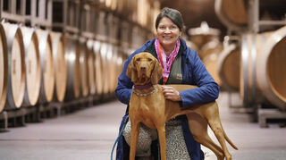 Kerstin Bauer hockt mit ihrem Spürhund Lea in einem Weinkeller des Weinguts von Winning.