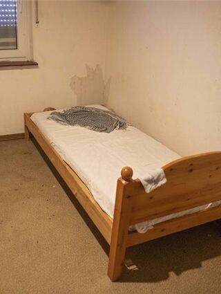Ein einzelnes Bett steht in einem abgewohnten Zimmer.