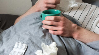 Mit Taschentüchern, Teetasse, Nasenspray und Tabletten im Bett liegen derzeit viele flach (gestellte Szene).