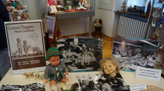 Im Mittelpunkt der diesjährigen Puppenausstellung steht das Jubiläum 150 Jahre Schildkrötfabrik. Auf dem historischen Foto rechts ist der Tisch einer ehemaligen Mitarbeiterin, Gerda Elm (2. von rechts), der Firma Schildkröt zur Bearbeitung der Puppen zu sehen.