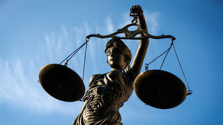 Eine Statue der Justitia hält eine Waage in ihrer Hand.