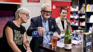 Wohl bekomm’s: Uwe Ittensohn stellt in der Buchhandlung Osiander sein neues Werk „Letzte Lese“ im Gespräch mit Bereichsleiterin Dagmar Strubl (l.) und Önologin Karoline Gaul (r.) vor und erläutert die Vier-Finger-Regel für Pfälzer Weinschorle.