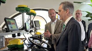 Der Manager des John Deere Forums, Heiner Ehmer (l.), erklärt dem US-Generalkonsul Norman Thatcher Scharpf (vorne) einen Landmaschinensimulator.