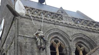 An der Kirche des Dorfes Sainte-Mère-Eglise erinnert eine Puppe an den US-Fallschirm-jäger John Steele, der am D-Day am Kirchturm hängenbleibt.