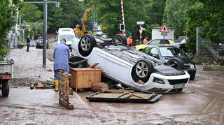 Auf einer Straße in Rudersberg liegt ein durch ein Hochwasser umgestürztes Auto auf dem Dach.