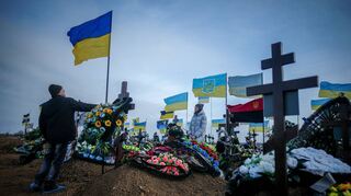 Angehörige getöteter Soldaten stellen an den Gräbern eine ukrainische Flagge auf.