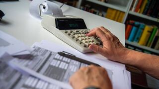 Ein Rentner füllt seine Steuererklärung fürs Finanzamt aus und tippt zur Berechnung Zahlen in einen Tischrechner.