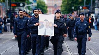 Polizisten tragen bei einem Trauermarsch für den bei einer Messerattacke tödlich verletzten Polizisten Rouven Laur dessen Bild.