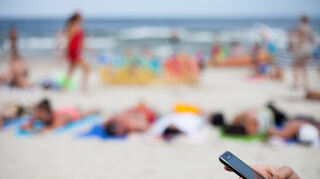Eine Frau hält ein Mobiltelefon am Strand an der Ostsee. Viele Berufstätige sind auch im Urlaub für die Arbeit erreichbar. (Symbolbild)