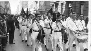 Musik für die Republik: Spielmannszug vom Reichsbanner Schwarz-Rot-Gold Mannheim in weißer Kleidung, aufgenommen zwischen den Quadraten P 4/Q 4 und P 3 /Q 3, sowie Zuschauer an beiden Straßenrändern im Jahr 1931.
