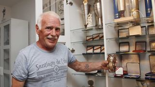 Fritz Nieblers Trophäensammlung füllt mehrere Vitrinen. In der Hand hält er den Olympia-Bären von Moskau, das Maskottchen der Spiele von 1980, die wegen der russischen Invasion in Afghanistan von vielen westlichen Nationen, darunter Deutschland, boykottiert wurden.