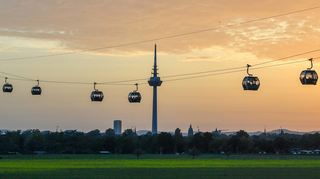 So ist sie in bester Erinnerung: die Seilbahn über der Feudenheimer Au und dahinter die Silhouette der Stadt Mannheim mit Fernmeldeturm.