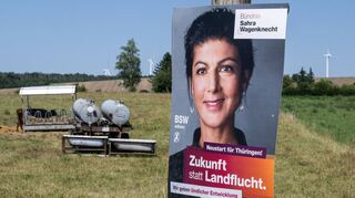 Ein Wahlplakat des BSW mit dem Slogan „Zukunft statt Landflucht“ hängt an einem Pfahl vor einer Wiese mit Kühen und Windrädern.