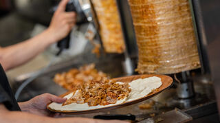 Ein Mitarbeiter einer Dönerbude legt Fleisch auf einen Yufka / Dürüm Döner.