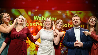 Denise Stripf (M), neu gewählte Pfälzische Weinkönigin, sowie ihre Stellvertreter, Manuel Reuther (r) und Lara Karr, stehen im Saalbau nach der Wahl und Krönung der "Pfälzischen Weinhoheiten" auf der Bühne. Hinter ihnen stehen die bisherigen Amtsträgerinnen, Weinprinzessin Hanna Spies (l-r), Weinkönigin Charlotte Weihl und Weinprinzessin Laura Götze.