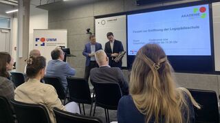 Finanzbürgermeister Volker Proffen (links auf dem Podium) hat Akademie-Direktor Marcus Hoffmann als Geschenk ein Bild vom Wasserturm mitgebracht.