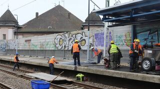 Am Bahnhof Mannheim-Neckarstadt tragen Bauarbeiter einen neuen Bahnsteigbelag aus Asphalt auf.