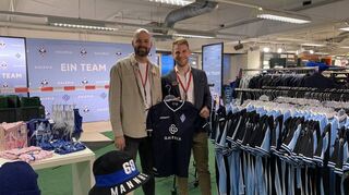 Abteilungsleiter André Schmahl (l.) und Galeria-Filialleiter Niko Rauch zeigen das neue Sondertrikot. Wer es kauft, erhält zwei Sitzplatzkarten gratis.