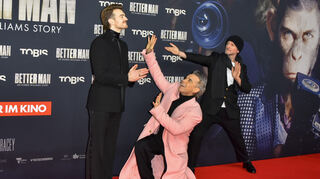 Robbie Williams (Mitte) bekniet bei der Kölner Premiere von „Better Man“ Hauptdarsteller Jonno Davies, angefeuert von Regisseur Michael Gracey.