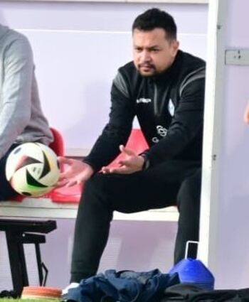 Betreuer Andreas Ganzinger sitzt auf einer Bank und fängt einen Fussball.