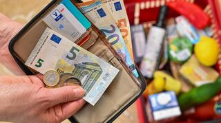 Eine Frau hält auf ihrer Hand Geld vor einem vollen Einkaufskorb mit Lebensmitteln. Viele Parteien versprechen mehr Geld im Geldbeutel.