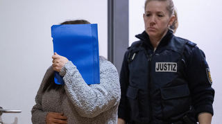Die wegen Mordes durch Unterlassung angeklagte Frau (l.) wird zum Auftakt des Prozesses im Landgericht Heidelberg von einer Justizbeamtin in den Gerichtssaal geführt.