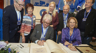 Marcel Reif trägt sich ins Goldene Buch der Stadt Bürstadt ein. Neben ihm sitzt Laudatorin Katrin Eigendorf. Landrat Christian Engelhardt (v.l.), Bürgermeisterin Bärbel Schader, Familienministerin Diana Stolz, Klaus Schlappner und Lars Reichow schauen zu.Bild: Berno Nix