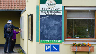 Fußgänger stehen hinter einer leeren Menükarte, die am Restaurant im Haus der Deutschen Weinstraße hängt.