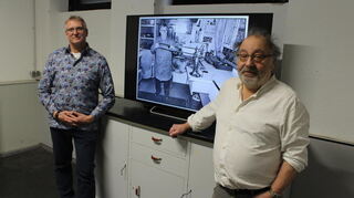 Die beiden Fotografen Bernhard Leibold (li.) und Frank Widmann (re.) neben einem Flachbildfernseher mit laufender Foto-Galerie.