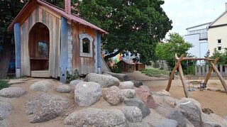 Eine Schaukel und Spielhäuser auf einem Spielplatz. Gerade in der Stadt sind Spielorte für Kinder unverzichtbar für ein gesundes Aufwachsen.