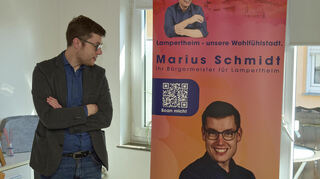 Marius Schmidt betrachtet sich auf einem Roll-Up, das zu Anfang des Wahlkampfs in seiner Wohnung für Veranstaltungen bereitsteht.
