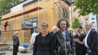 Ein ungewöhnlicher Ort für Kunst findet gerade seinen dritten Standort: Das Einraumhaus auf dem Alten Meßplatz in Mannheim. Vorne die beiden Kunstschaffenden Myriam Holme und Philipp Morlock beim Richtfest.