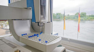Ein Laborgerät zur Prüfung der Wasserqualität steht bei einem Rundgang durch die Rheingütestation vor einem Fenster mit Blick auf den Rhein.