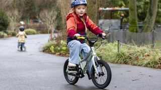 Kind fährt auf einem Kinderfahrrad durch einen Park.