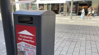 Der neue Pizzakarton-Mülleimer auf den Planken steht auf Höhe O6 gegenüber eines Pizza-Restaurants.