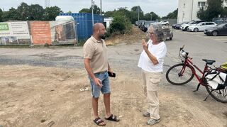 Grünen-Fraktionschefin Gabriele Baier mit Anwohner Fatih Alkan vor dem Bauzaun des umstrittenen Lager-Komplexes am Riestenweg im Mannheimer Stadtteil Hochstätt.