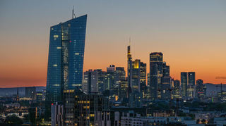 Die Lichter der Bankentürme von Frankfurt leuchten in der hereinbrechenden Dunkelheit, die EZB (l.) dominiert die Skyline.