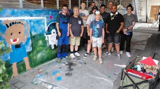 Graffiti-Künstler „Rise One“ (3. v. r.) gestaltete mit zehn Teilnehmenden mit und ohne Behinderung zwei Betonwände in der Wohneinrichtung am Falterweg.