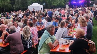 Auch auf den Bierbänken vor der Bühne frönen die Menschen den Annehmlichkeiten des Abends beim Sommerfest am See in Heddesheim.