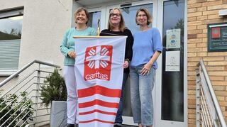 Claudia Dewald-Haas, Jeanette Schneider und Pressereferentin, Claudia Betzholz halten die Fahne der Caritas hoch.