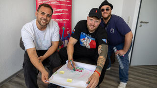 Rapper Finch unterschreibt auf der Glücksgefühle-Zeitungsseite – zur Freude von Volontär Noah Eschwey (l.) und Redakteur Henrik Feth (r.).