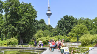 Der Fernmeldeturm davor Seerosen und Besucher beim Festakt Parkjubiläum zu 50 Jahre Stadtparks im Baumhain im Luisenpark Mannheim.