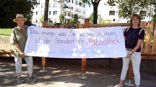 Kristin Hätterich (l.) und Martina Kutscher-Bauer vom Förderverein der Stadtteilbibliothek protestieren mit einem Banner bei einer Spielplatzeröffnung in Friedrichsfeld.