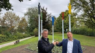 Künstler Bernd Gerstner und Bürgermeister Achim Weitz stoßen auf die Eröffnung des Skulpturenwegs am Badesee an. Die Säulen im Hintergrund stammen aus historischen Heddesheimer Gebäuden, die Figuren prosten sich zu.