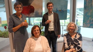 Künstlerin Helga Lavi (links stehend), der Geschäftsführer der Biedensand Bäder Marius Schmidt und Besucherinnen der Ausstellung.