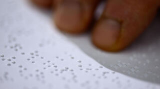 Ein Mitarbeiter des Deutschen Zentrums für barrierefreies Lesen (DZB Lesen) liest in der Druckerei einen Text in Brailleschrift.